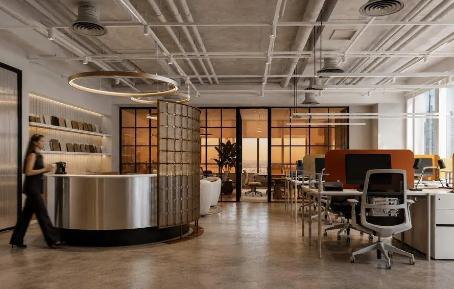 Curved brushed-steel reception desk under copper ring pendants, open office beyond