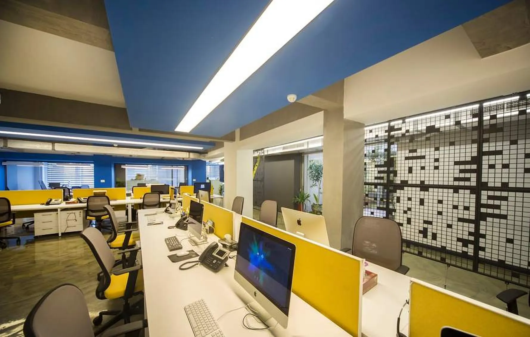 Open office with yellow desk screens under a blue ceiling